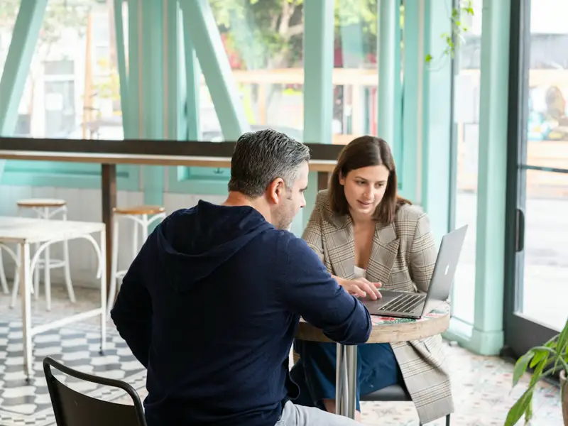Two people working together at a laptop in a café.